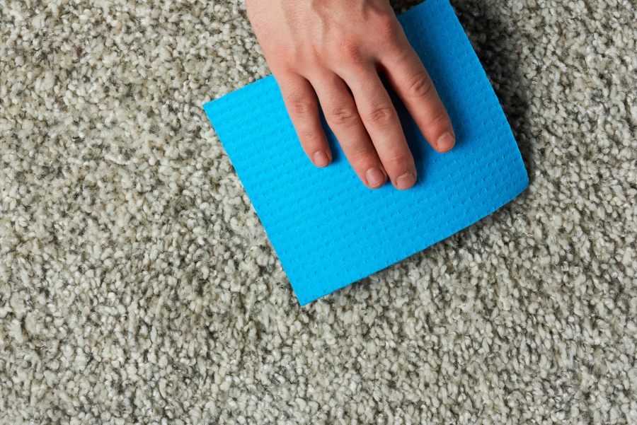 Blaues Schwammtuch nimmt Fleck vom Teppich auf